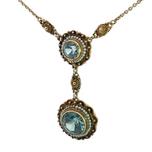 Load image into Gallery viewer, Introducing the Victorian 14kt Yellow Gold 5.50cttw Blue Zircon + Seed Pearls Pendant: a vintage masterpiece featuring an ornate design with two round blue zircons elegantly set in intricate gold filigree. These stunning gemstones are connected by small gold links and accented with delicate seed pearls, creating a cohesive and refined look. The pendant is supported by a delicate chain, offering an elegant antique appearance that captures timeless beauty.