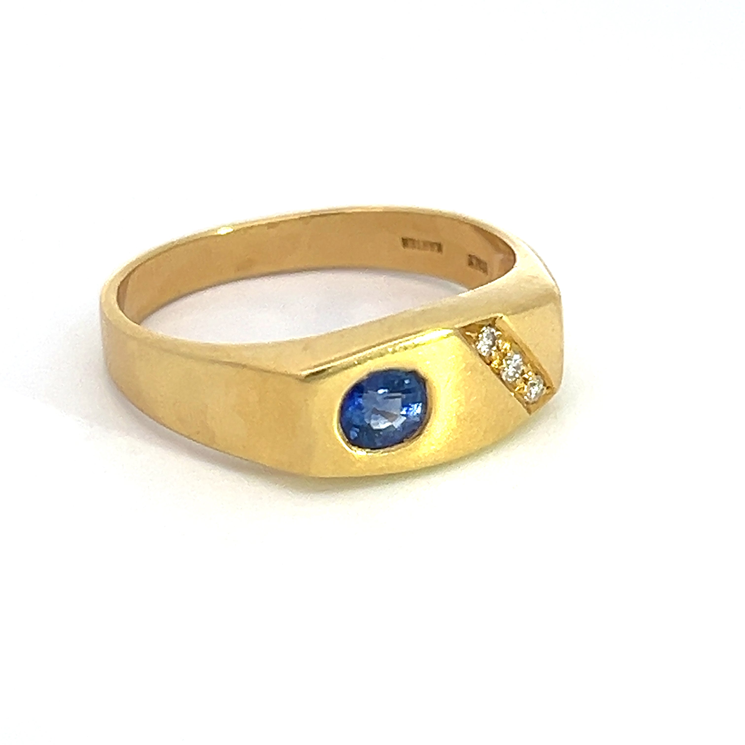 The Mid Century 18k yellow gold ring features a .50ct sapphire gemstone positioned on the left side, complemented by three .15cttw diamonds diagonally aligned on the right side of the band, all set against a plain white background.
