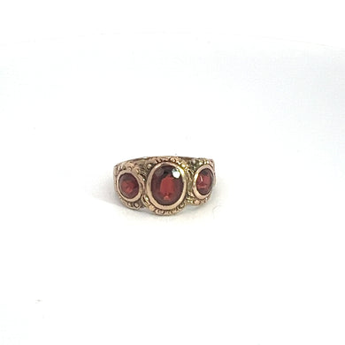 The Victorian 10kt Yellow Gold 5.50ct Garnet Ring showcases three large, deep red garnets in a row, with the central gemstone being the largest and flanked by slightly smaller gems on each side. The ring features intricate detailing around the band, reminiscent of Victorian jewelry, enhancing its ornate appearance against a plain white background.