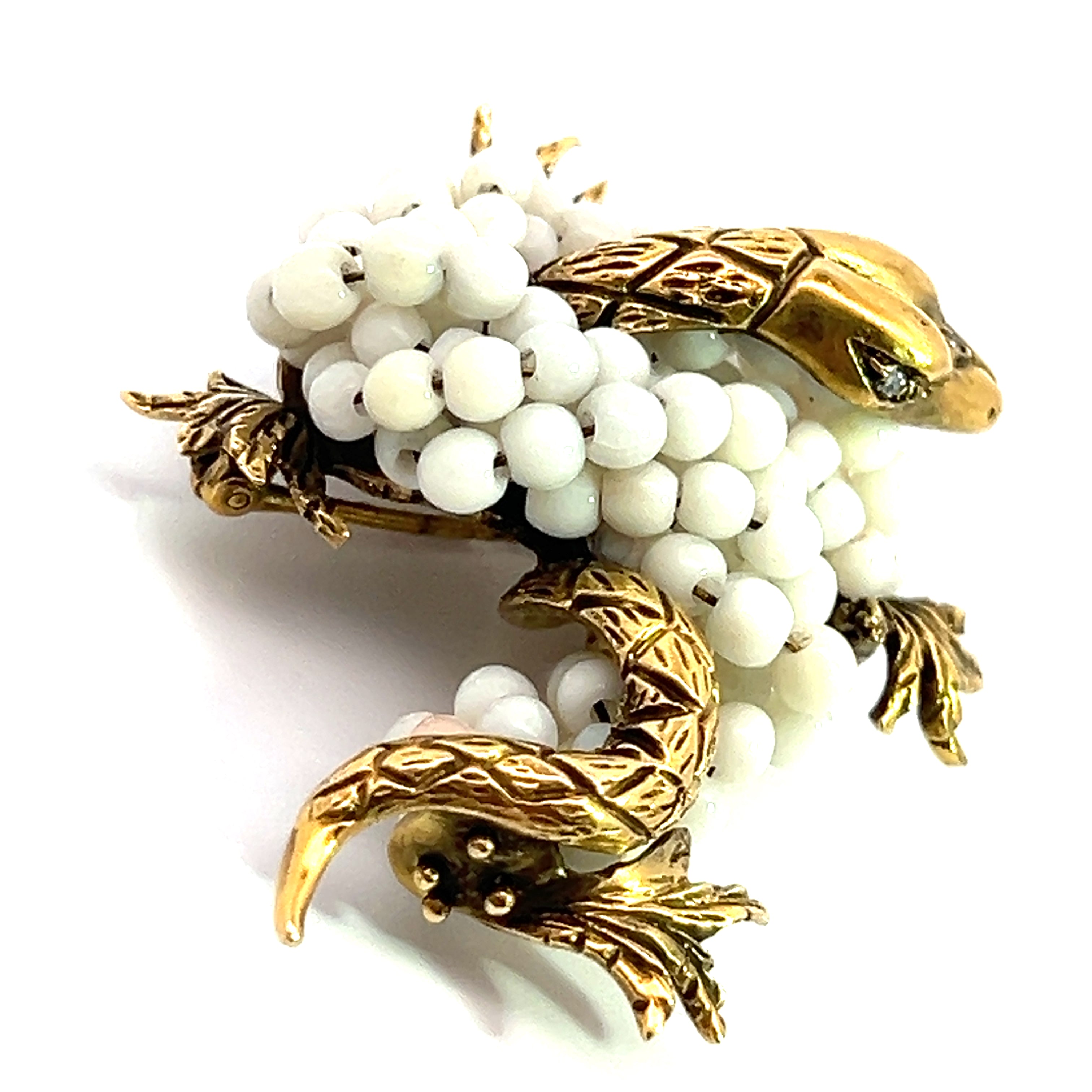 The "Mid Century 14kt Yellow Gold Coral + .03ct Diamond Dragon Brooch" showcases a golden head, legs, and tail adorned with white bead embellishments. The detailed scales and leaves further enhance its intricate and elegant appearance, reminiscent of a classic Mid Century brooch.