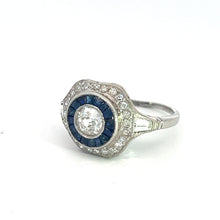 Load image into Gallery viewer, The Art Deco Platinum .65ct Old Mine Cut Diamond + 1cttw Sapphires + 1.50cttw Diamonds Ring boasts an intricate design with a prominent large central old mine cut diamond, encircled by smaller blue sapphires and an outer band of tiny diamonds. This vintage-style ring is elegantly displayed against a plain white background.