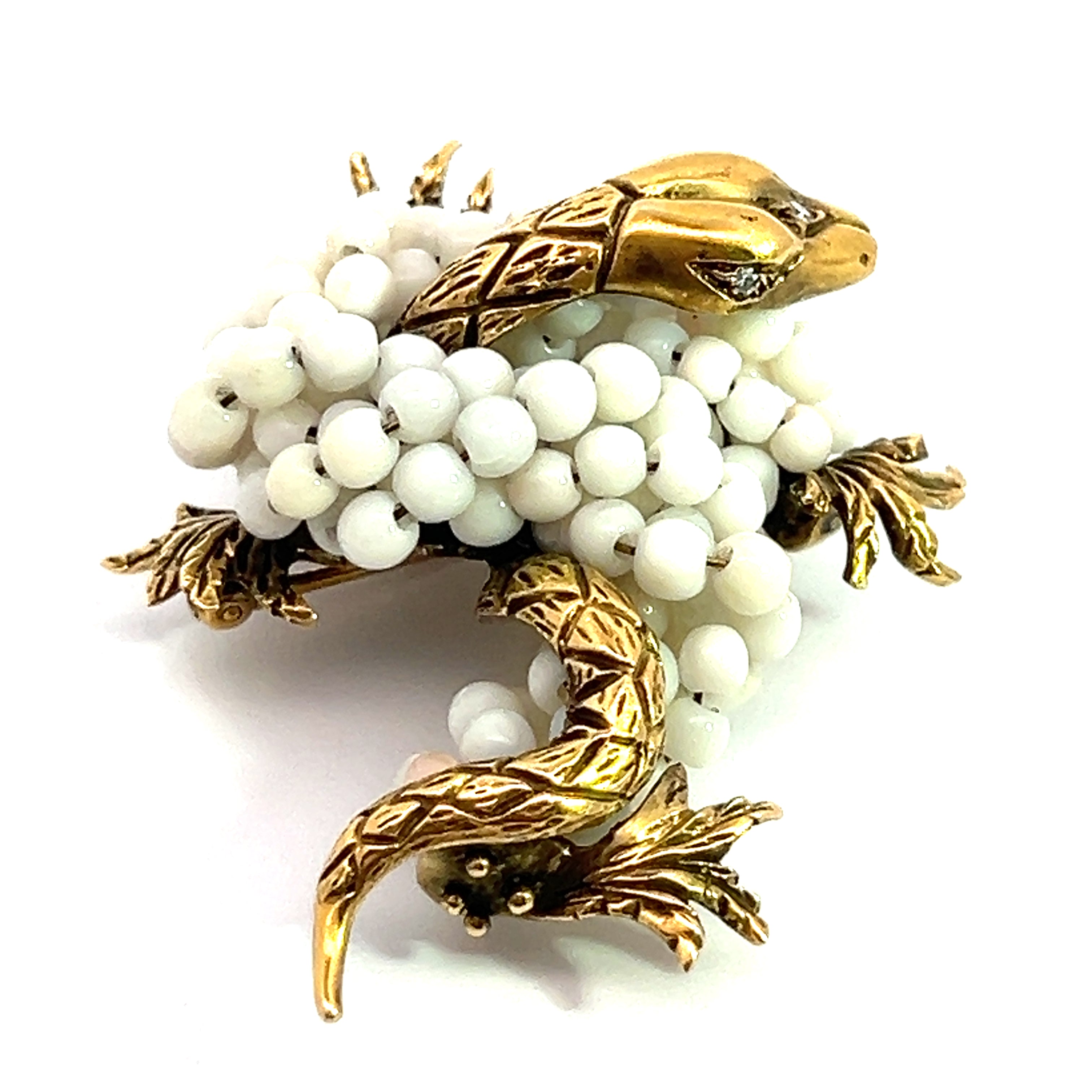 The "Mid Century 14kt Yellow Gold Coral + .03ct Diamond Dragon Brooch" showcases a golden head, legs, and tail adorned with white bead embellishments. The detailed scales and leaves further enhance its intricate and elegant appearance, reminiscent of a classic Mid Century brooch.