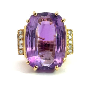 The Late Century 14kt yellow gold ring showcases a striking 33-carat rectangular-cut amethyst with softened corners. This magnificent centerpiece is flanked on either side by sections embellished with rows of small white diamonds totaling .70 carats. The exquisite diamond and amethyst ring is beautifully set against a plain white background.