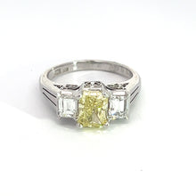 Load image into Gallery viewer, The Modern Platinum 1.29ct Fancy Yellow Radiant Cut Diamond + .66cttw Emerald Cut Diamond Ring showcases a stunning 1.29ct radiant cut fancy yellow diamond at its center, complemented by two rectangular clear emerald cut diamonds on either side. The ring band features sleek and elegant cuts, enhancing its overall sophistication.