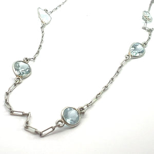 A delicate 20-inch Mid Century Platinum necklace, showcasing approximately 5 carats of aquamarines in a mix of teardrop and round settings, with each gemstone evenly spaced along the chain made up of smooth, flat, interlocking links.