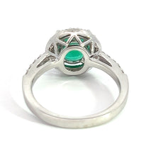 Load image into Gallery viewer, The Modern 18kt White Gold 1.80ct Emerald + .50cttw Diamond Ring is shown from the perspective standing on its band. Crafted in 18kt white gold with an intricate setting featuring a central 1.80ct emerald, the ring&#39;s open design beneath the gemstone allows light to pass through, enhancing its elegant and refined appearance.