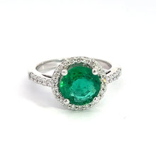 Load image into Gallery viewer, The Modern 18kt White Gold 1.80ct Emerald + .50cttw Diamond Ring showcases a stunning silver band adorned with small diamonds, creating a sparkling, elegant appearance against a plain white background. This exquisite piece features a large, 1.80ct round emerald at its center, surrounded by a halo of .50cttw small white diamonds and is crafted from luxurious 18kt white gold.