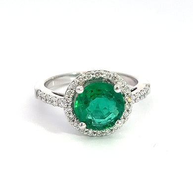 The Modern 18kt White Gold 1.80ct Emerald + .50cttw Diamond Ring showcases a stunning silver band adorned with small diamonds, creating a sparkling, elegant appearance against a plain white background. This exquisite piece features a large, 1.80ct round emerald at its center, surrounded by a halo of .50cttw small white diamonds and is crafted from luxurious 18kt white gold.