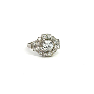 A detailed platinum ring featuring a prominent central hexagonal clear gemstone (0.95ct Old European Cut), surrounded by smaller diamonds (1.28cttw) arranged in a geometric pattern. This Art Deco Platinum Diamond Ring exudes vintage sophistication, with the intricate design and sparkle of the stones standing out on a white background.