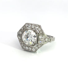 Load image into Gallery viewer, An Art Deco Platinum 2ct Old European Cut Diamond ring, featuring a large, round-cut diamond in the center. The central diamond is encircled by smaller diamonds in an octagonal setting and adorned with additional diamond accents on the band. This exquisite vintage-style ring is showcased against a plain white background.