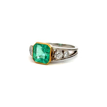 Load image into Gallery viewer, The Mid Century Platinum &amp; 18kt Yellow Gold 4.03 Emerald Cut Emerald + .70cttw Diamond Ring showcases an elegant design with a large, 4.03ct emerald-cut green gemstone set in a gold bezel. The sophisticated platinum band is adorned with three round diamonds on each side of the central stone, exuding Mid Century flair, and is photographed against a plain white background.