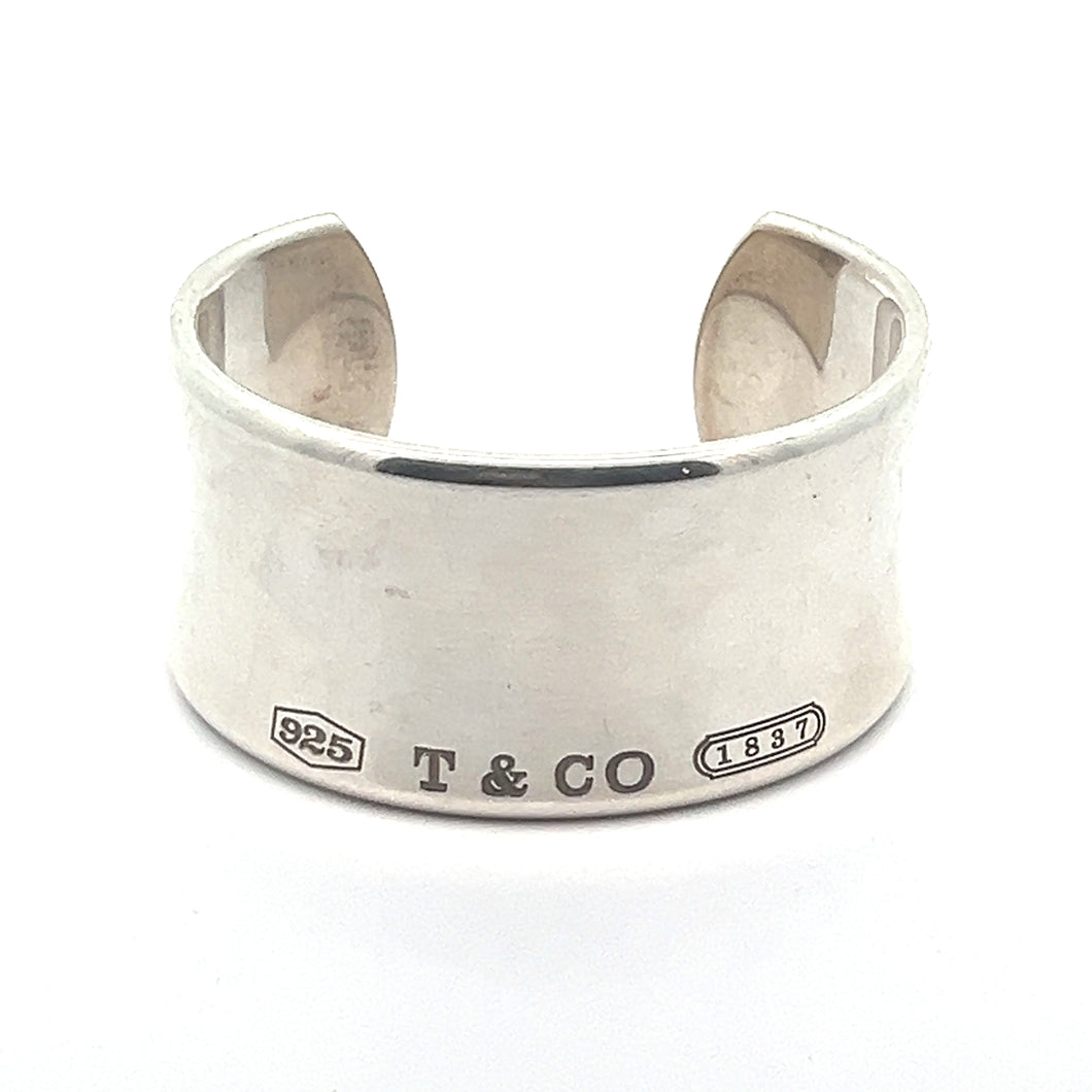 A wide-cuff ring in silver with a split at the back, prominently displaying the engravings 