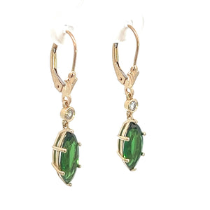 The Modern 14kt Yellow Gold 4cttw Tsavorite Garnet + .10cttw Diamond Earrings display a pair of elegant drop earrings featuring vibrant green marquise-cut stones, each accented by a small round clear diamond above the main gem. These stunning earrings are shown hanging, highlighting their clasp hooks and detailed metalwork.