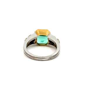 Product: The Mid Century Platinum & 18kt Yellow Gold ring features a stunning twin-stone setting with a 4.03ct emerald cut emerald next to .70cttw diamonds, exuding sophistication and elegance. Its smooth and elegant band enhances the classic allure of the gemstones against a plain white background.