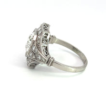 Load image into Gallery viewer, The Art Deco Platinum 2ct Old European Cut Diamond + .84cttw Diamond Ring, featuring an intricate filigree design on the band, is adorned with a large central gemstone and smaller surrounding stones set in white metal. Displayed against a white background, it exemplifies detailed craftsmanship with an elegant, timeless appearance.