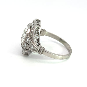 The Art Deco Platinum 2ct Old European Cut Diamond + .84cttw Diamond Ring, featuring an intricate filigree design on the band, is adorned with a large central gemstone and smaller surrounding stones set in white metal. Displayed against a white background, it exemplifies detailed craftsmanship with an elegant, timeless appearance.