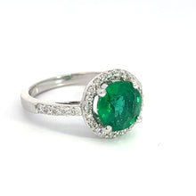 Load image into Gallery viewer, Presenting the Modern 18kt White Gold 1.80ct Emerald + .50cttw Diamond Ring, a stunning piece that showcases a large, round 1.80ct emerald at its center, encircled by .50cttw sparkling diamonds. The elegant and luxurious 18kt white gold band is further adorned with small diamonds, enhancing its beauty. The ring is elegantly displayed against a plain white background.