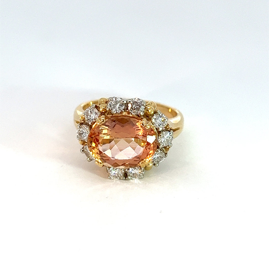 The Late Century 18ktyg 4.30ct Imperial Topaz + .75cttw diamond ring showcases a large, oval-cut, peach-colored Imperial Topaz at its center, surrounded by smaller round diamonds in a halo pattern. The smooth and polished 18k Yellow Gold band epitomizes Late Century glamour against a plain white background.