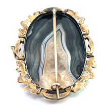 Load image into Gallery viewer, An ornate vintage piece named the Victorian 10ktyg Banded Agate + Quartz Crystal Pendant/Pin showcases an oval-shaped banded agate gemstone with patterns in shades of black, white, and beige. This Victorian jewelry is set within an intricate gold-toned metal frame and secured with a vertical pin on the back.
