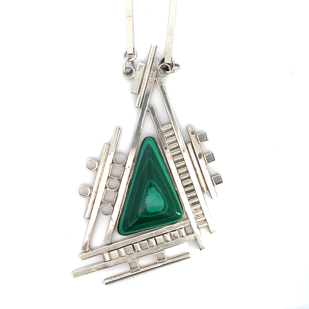 The 1995 sterling silver Aaron Rubenstein malachite geometric necklace, measuring 22 inches, showcases a unique abstract design with geometric lines and shapes. The triangular pendant incorporates circles and rectangles, highlighting a large, polished malachite gemstone at its center. This luxurious piece of jewelry hangs elegantly from a thin silver chain.