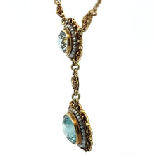 Load image into Gallery viewer, A close-up view of the Victorian 14kt Yellow Gold 5.50cttw Blue Zircon + Seed Pearls Pendant showcases two circular pendants highlighted by light blue zircons, encircled with gold and adorned with miniature seed pearls. The pendants are elegantly connected by delicate, intricate gold links forming a graceful design.