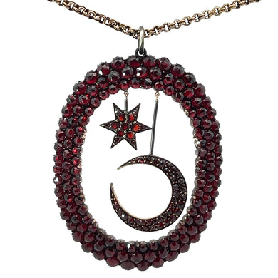 The Victorian Vermeil Star & Moon Large Pendant, encrusted with dark red gemstones and surrounded by an oval border adorned with the same red gems, hangs beautifully from a 21-inch 15kt yellow gold Victorian chain, capturing celestial motifs perfectly.