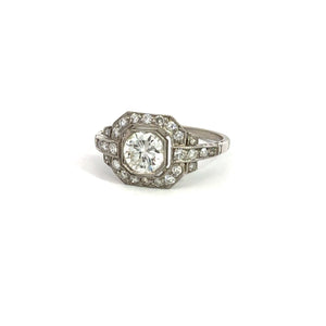 The Late Art Deco Platinum .91ct Round Brilliant Cut Diamond + 1.16cttw Diamond Ring exudes vintage sophistication and Art Deco elegance with its large round central diamond set in an intricate geometric design, surrounded by smaller diamonds, all beautifully showcased against its white background display.