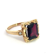 Load image into Gallery viewer, Introducing the Mid Century 14ktyg 4.80ct Garnet + .06cttw Diamond Ring: this exquisite piece showcases a large, rectangular, dark red garnet gemstone of 4.80 carats at its center, elegantly held by an ornate and intricately detailed setting that draws inspiration from mid-century design. A small clear diamond of .06 carat total weight is set on the band beside the main setting, all presented against a plain white background.