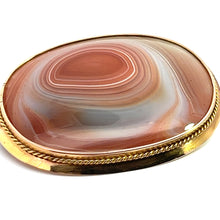 Load image into Gallery viewer, A Victorian-style brooch, named the Victorian 14ktyg Large Banded Agate Pin, features an oval-shaped polished surface with a multi-hued concentric pattern in shades of brown, white, and beige. This exquisite pin is bordered with a 14kt yellow gold frame, adding an elegant contrast to the intricate design of the natural stone.