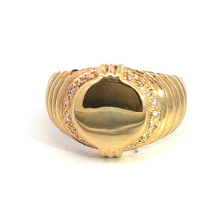 The Late Century 14ky Yellow Gold .24cttw Signet Ring showcases an oval-shaped central piece with a smooth, reflective surface. Surrounding the oval is a border of small, sparkling diamonds that enhance the ring's elegant and luxurious appearance. The band features polished, grooved lines that make it a perfect addition to any fine jewelry collection.