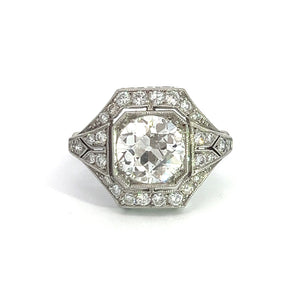 Introducing the Art Deco Platinum 2ct Old European Cut Diamond + .84cttw Diamond Ring, a vintage masterpiece showcasing an elaborate design. At its heart sits a large central round diamond, encircled by a geometric halo of smaller diamonds, all set in a beautifully detailed and ornate band. The octagonal setting is meticulously crafted to embody Art Deco elegance, featuring intricate side details against a pristine white backdrop.