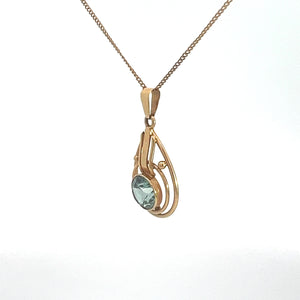 The Art Nouveau 14kt Yellow Gold 2ct Blue Zircon Necklace showcases a delicate pendant with an elegant open swirl design, encasing a light blue zircon gemstone. This stunning pendant is suspended from a fine gold chain against a plain white background.