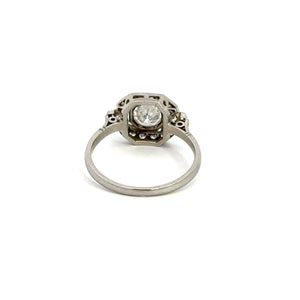 The Art Deco Platinum .80ct Round Brilliant Cut + 1.08cttw Diamond Ring features a round brilliant cut diamond set in a geometric bezel setting. The ring's band is simple and unadorned, directing attention to the central diamond. The overall design exudes a vintage Art Deco aesthetic, beautifully showcased against a plain white background.