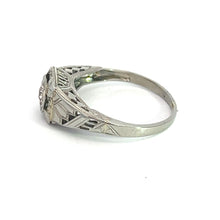 Load image into Gallery viewer, The Art Deco 18ktwg .20ct Old European Cut Diamond Filigree Ring, displayed on a white background, showcases a central Old European Cut Diamond set in an 18kt white gold band with intricate engravings. The ring features detailed patterns along the sides, highlighting the craftsmanship of its design.