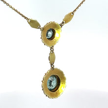 Load image into Gallery viewer, The Victorian 14kt Yellow Gold 5.50cttw Blue Zircon + Seed Pearls Pendant features a gold chain adorned with two ornate, round gold settings, each showcasing a stunning blue zircon gemstone at the center. The pendants are connected by delicate gold links and are embellished with intricate leaf-like gold decorations and seed pearls.