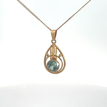 Load image into Gallery viewer, An Art Nouveau 14kt yellow gold necklace with a delicate chain featuring a teardrop-shaped pendant. The pendant has an open geometric design and holds a single, round blue zircon gemstone at its center. The background is white.