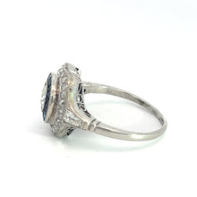 Load image into Gallery viewer, An Art Deco Platinum .65ct Old Mine Cut Diamond + 1cttw Sapphires + 1.50cttw Diamonds Ring is displayed on its side, showcasing a large central gemstone surrounded by smaller diamonds. The ring band features delicate filigree detailing, reminiscent of the Art Deco era. The plain white background emphasizes the ring&#39;s exquisite details.