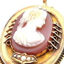 Load image into Gallery viewer, A close-up image of the Victorian 14ktyg Carved Agate Portrait of a Lady Cameo brooch. This exquisite piece showcases a white carved profile of a woman with detailed hair and clothing, set against a reddish-brown background. The cameo is framed in ornate 14kt yellow gold, featuring decorative elements and adorned with a row of pearls at the bottom.