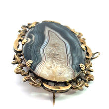 Load image into Gallery viewer, An intricate Victorian 10ktyg banded agate and quartz crystal pendant/pin featuring an oval-shaped, banded agate stone set in a beautifully detailed gold-toned frame. Reflecting the elegance of Victorian jewelry, this piece comes with a pin clasp on the back. The agate stone showcases natural banded patterns in enchanting shades of gray, white, and tan.