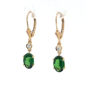 These earrings, named the "Modern 14kt Yellow Gold 2.25ct Tsavorite Garnets + .10cttw Diamond Earrings," feature elegant drop designs with 14kt yellow gold hooks. Each earring showcases a small, round diamond set above a larger, oval-shaped Tsavorite Garnet. The gemstones are secured with prongs in a stylish gold setting.