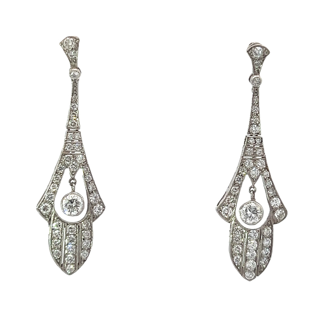 The Late Art Deco Platinum 4.12cttw Diamond Dangle Earrings are a pair of elegant, elongated drop earrings encrusted with small diamonds. Each earring features a central round diamond set in a decorative, intricate design with additional diamond accents throughout, boasting a vintage, art-deco style.