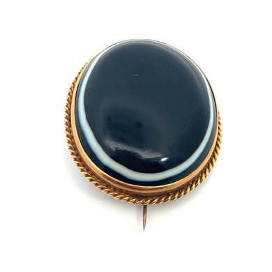 The Victorian 22kt Yellow Gold Bullseye Agate Brooch showcases a polished black onyx stone, elegantly encased in a golden, rope-style border. Crafted from 22kt yellow gold, it features a simple pin clasp at the back for fastening.