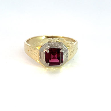 The Art Deco 14kt Two Tone Gold 1ct Rubelite Tourmaline Ring boasts an ornate band with intricate engraved detailing. It features a square-shaped, 1ct Rubelite Tourmaline encased in a silver-colored bezel. The background is plain and white.