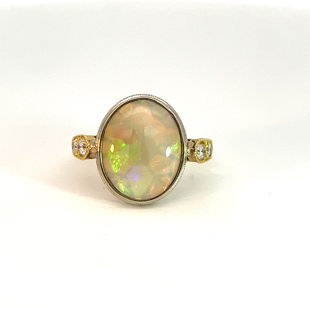 A close-up of the Mid Century 18kt 2 tone 3.62 Opal + .21cttw Dia ring showcasing its large, iridescent oval-shaped opal stone. The opal is elegantly set in an 18kt two-tone band, accented by small diamonds on either side. The smooth white background highlights the ring's intricate details beautifully.