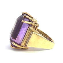 Load image into Gallery viewer, The Late Century 14ktyg 33ct Amethyst + .70cttw Diamond Ring showcases a sizable rectangular amethyst held securely by four prongs. This exquisite piece features a wide band with a smooth finish and a slightly raised setting that highlights the gemstone&#39;s facets and vibrant color, displayed at an elegant angle.