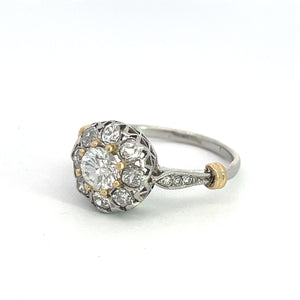 An exquisite Edwardian Platinum & 18kt Yellow Gold 1.30cttw Old Mine Cut Diamond Ring showcasing a central round diamond encircled by a halo of smaller diamonds, set in an intricately designed vintage-inspired platinum and yellow gold band. The ring is displayed on a plain white background.