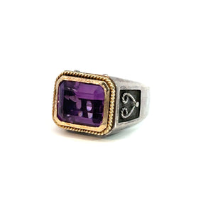 The Late Century Konstantino Sterling Silver & 18kt Yellow Gold 5ct Emerald Cut Amethyst Ring showcases a substantial, rectangular purple gemstone encased in elegant 18kt yellow gold accents. This exquisite piece is adorned with an intricate design on the sterling silver band, featuring detailed metalwork on either side of the amethyst. The vivid ring is set against a white background.