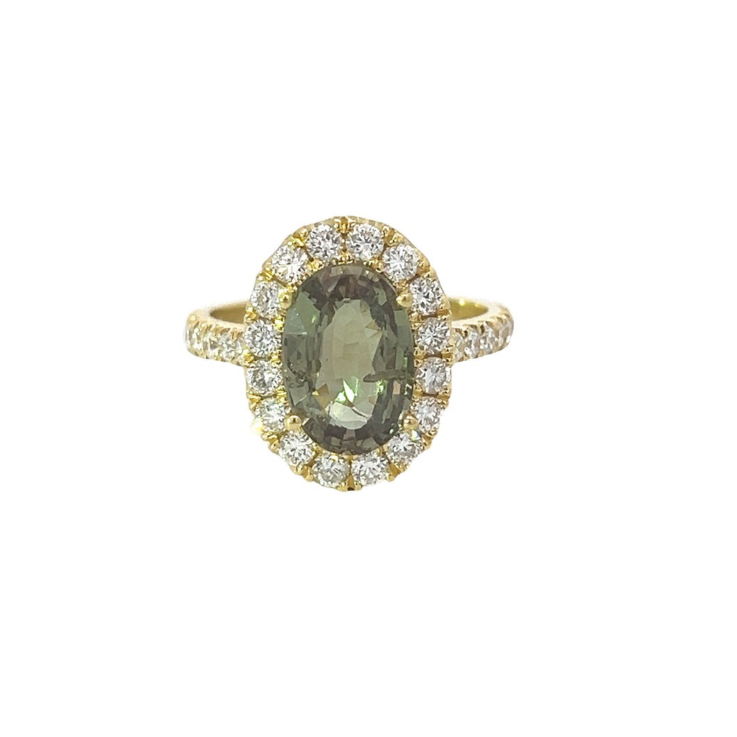 A gold ring boasting a 3.55-carat oval-shaped natural Sri Lankan Alexandrite at the center, encircled by a halo of round brilliant cut diamonds totaling 1.30 carats. The 18kt two-tone gold band, also adorned with diamonds, rests on a white background that highlights its intricate details. This Modern 18kt Two-Tone Gold Alexandrite Ring exudes elegance and refined craftsmanship.