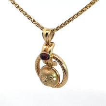 Load image into Gallery viewer, The Victorian 14kt yellow gold pendant features a detailed twisted chain and showcases a classic circular locket adorned with engraved stars and accented by a small, oval-shaped Cabochon Garnet at the top. This exquisite locket, weighing .50 carats, hangs from an interlocked double-ring design on an 18-inch chain against a white background.