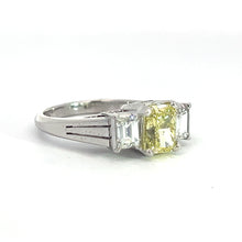 Load image into Gallery viewer, The Modern Platinum 1.29ct Fancy Yellow Radiant Cut Diamond + .66cttw Emerald Cut Diamond Ring boasts a central radiant cut fancy yellow diamond weighing 1.29 carats, flanked by two smaller emerald cut clear diamonds on either side, all set within a sleek and simple band. The ring is beautifully presented against a plain white background in the photograph.